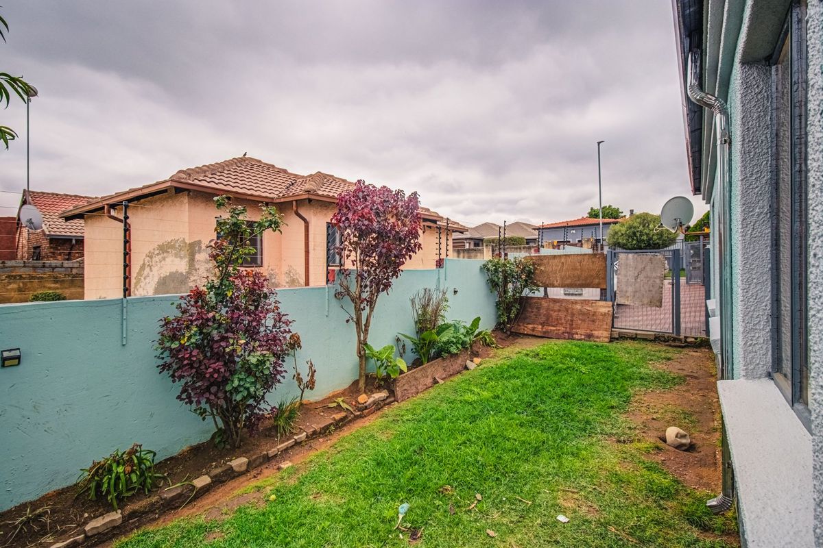 A rear garden area featuring a boundary wall with electric fencing, a metal gate, and a small lawn section.