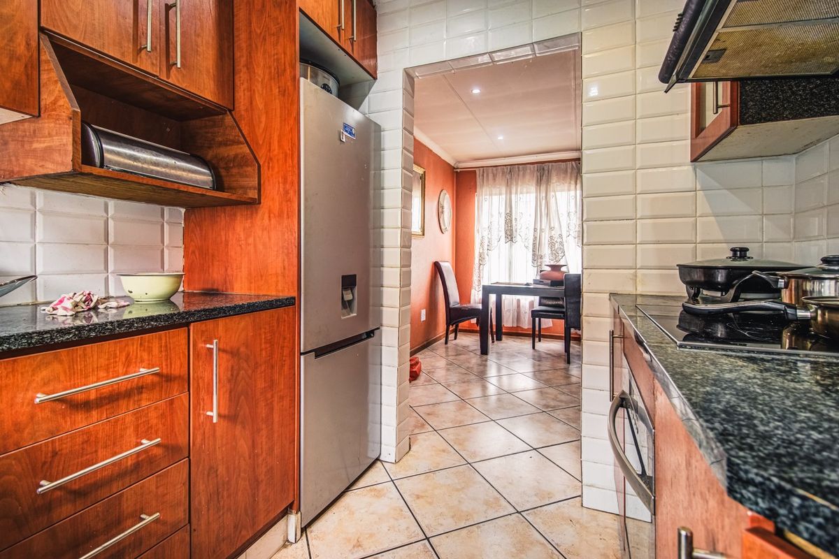 A functional kitchen featuring warm-toned wooden cabinetry, granite countertops, and a tiled backsplash, leading into an adjacent dining area.