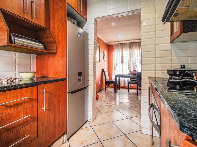 A functional kitchen featuring warm-toned wooden cabinetry, granite countertops, and a tiled backsplash, leading into an adjacent dining area.