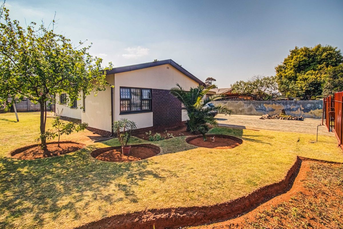 Rear view of the property featuring a landscaped garden, paved driveway, and secure brick boundary wall.