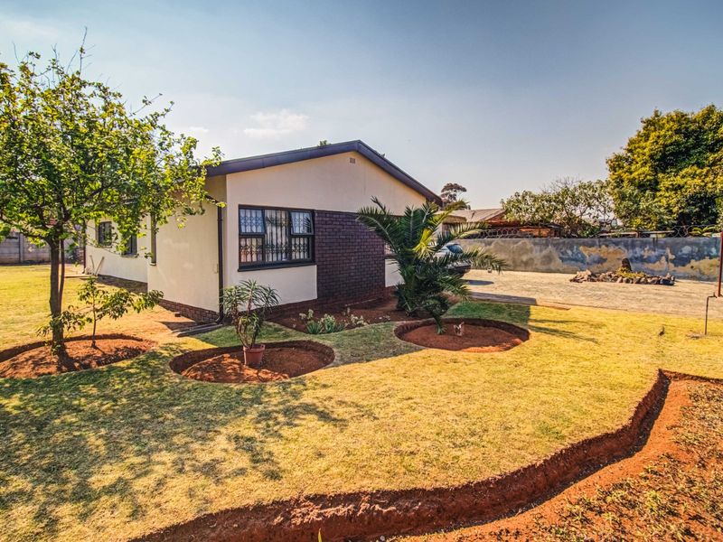 Rear view of the property featuring a landscaped garden, paved driveway, and secure brick boundary wall.