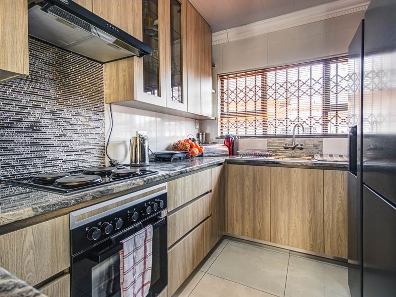 Modern kitchen featuring wood-finish cabinetry, stone countertops, a mosaic tile backsplash, and integrated appliances including an oven and hob.