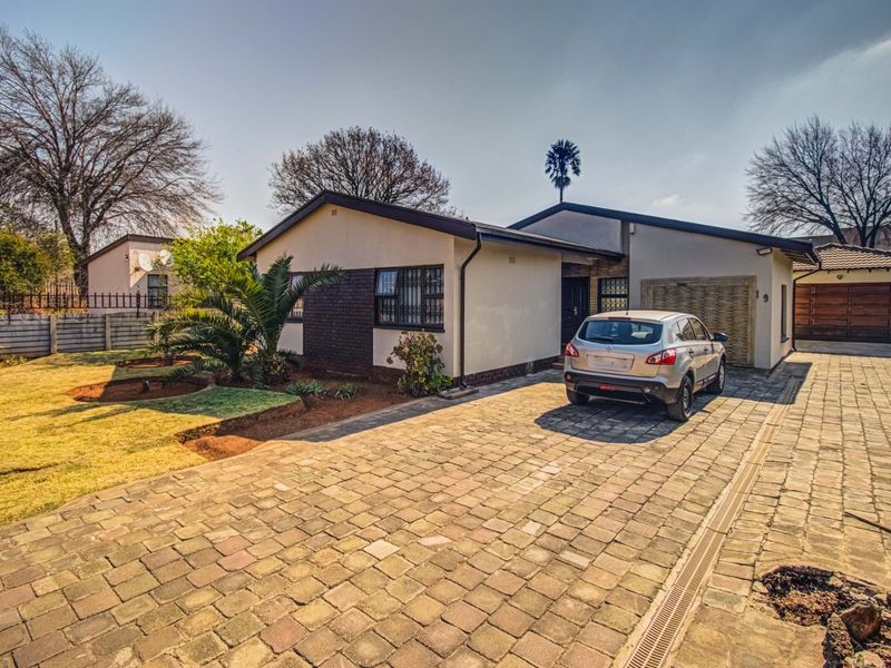 Front view of a single-story house featuring a paved driveway, brick and plaster facade, and secure garage access.