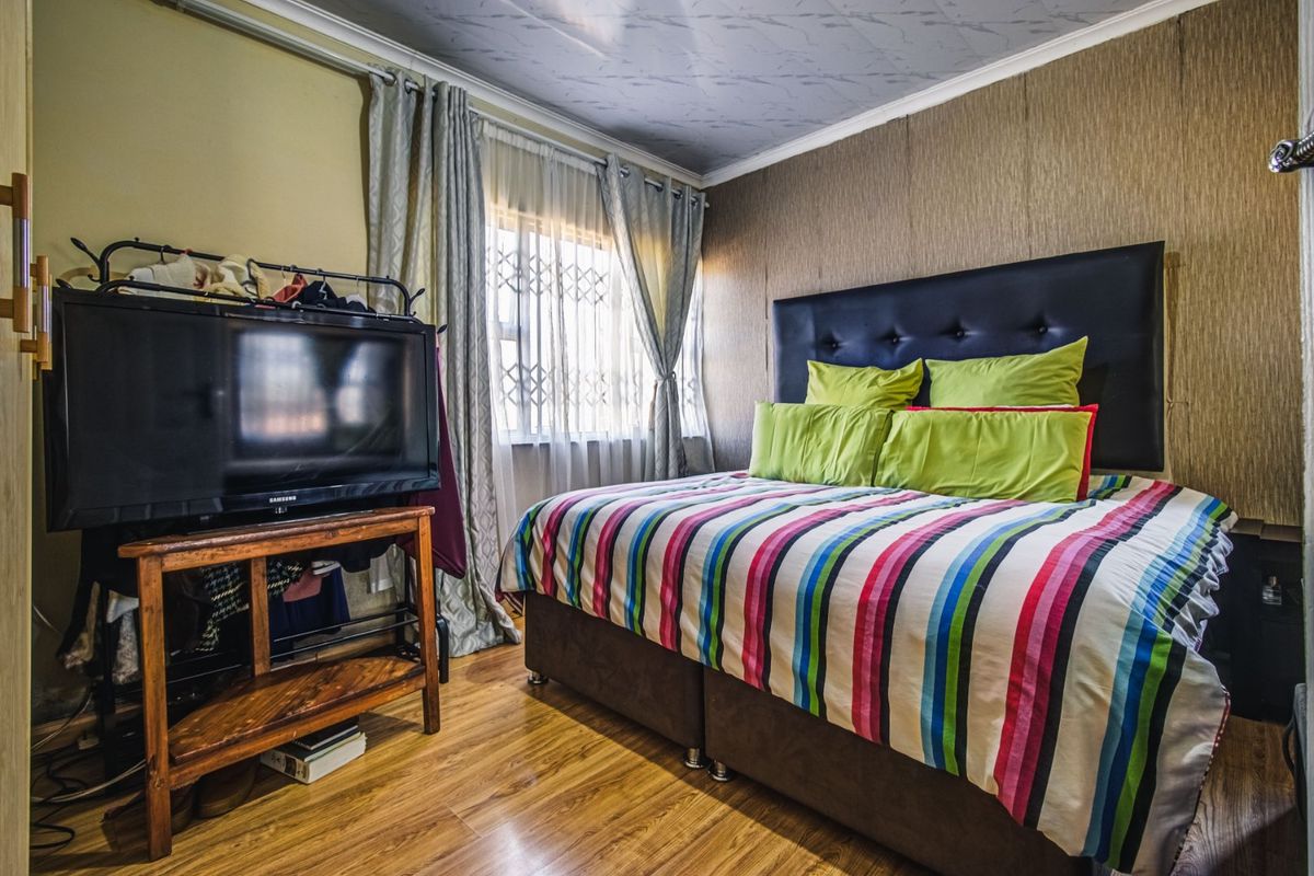 A bedroom featuring laminate flooring, textured wall finishes, and a security gate on the window.
