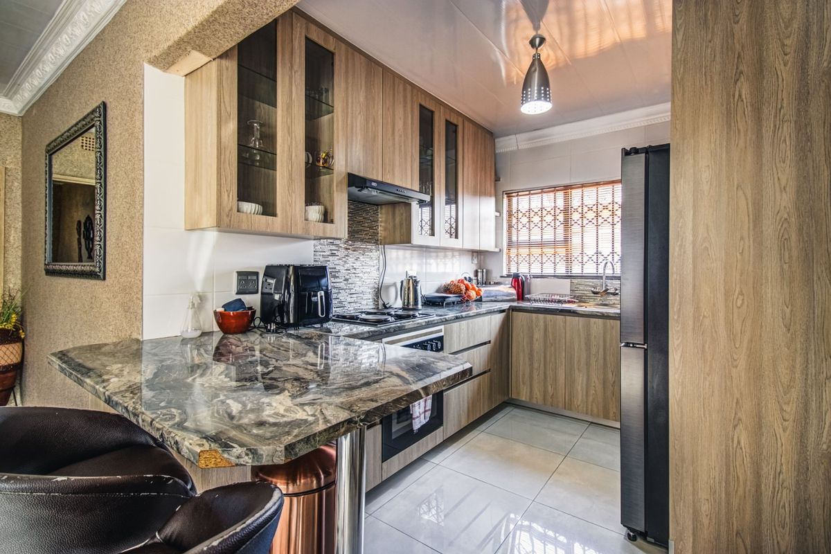 A modern kitchen featuring wood-finish cabinetry, stone countertops, a breakfast bar, and integrated appliances, complemented by tiled flooring and a tiled backsplash.