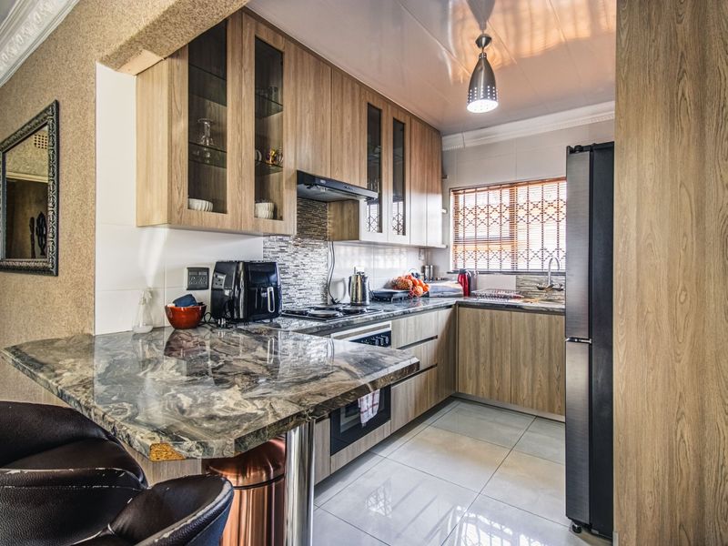 A modern kitchen featuring wood-finish cabinetry, stone countertops, a breakfast bar, and integrated appliances, complemented by tiled flooring and a tiled backsplash.