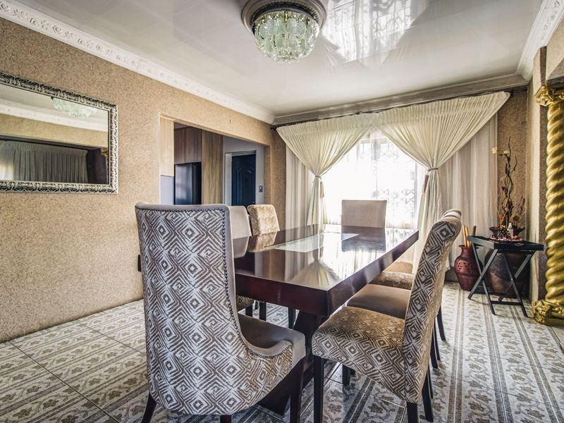A formal dining room featuring tiled flooring, a decorative ceiling cornice, a crystal chandelier, and a unique decorative pillar.
