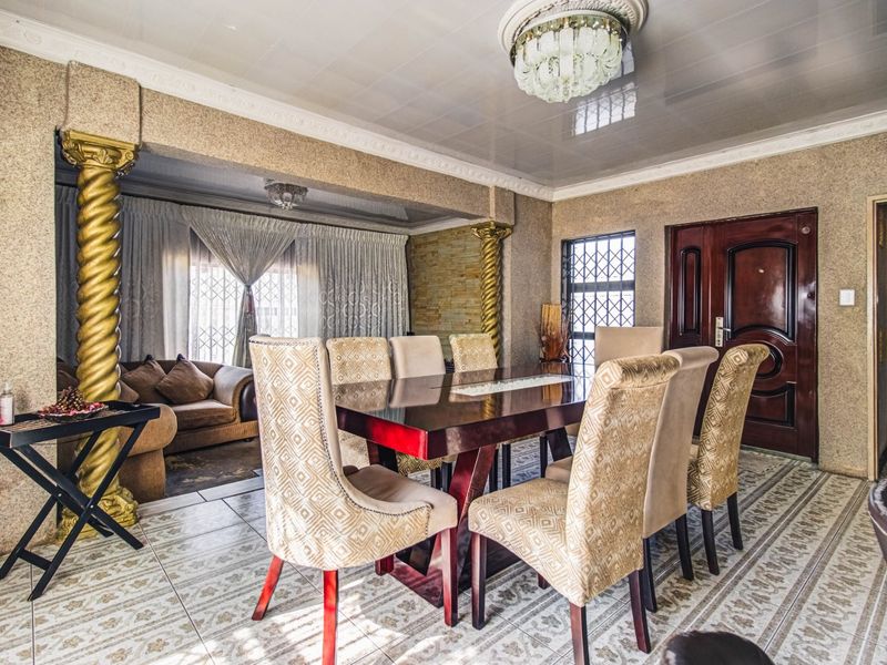 Spacious dining area featuring decorative gold columns, glossy ceiling finish, and patterned ceramic floor tiles, creating a distinct and formal atmosphere.