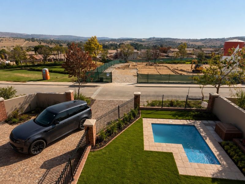 Aerial view of a residential property featuring a private swimming pool, paved driveway, and landscaped garden with perimeter fencing.