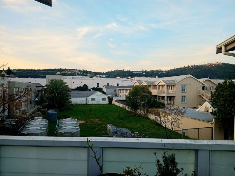 An elevated view overlooking a suburban landscape with neighboring buildings, green space, and water storage tanks, captured from a balcony.