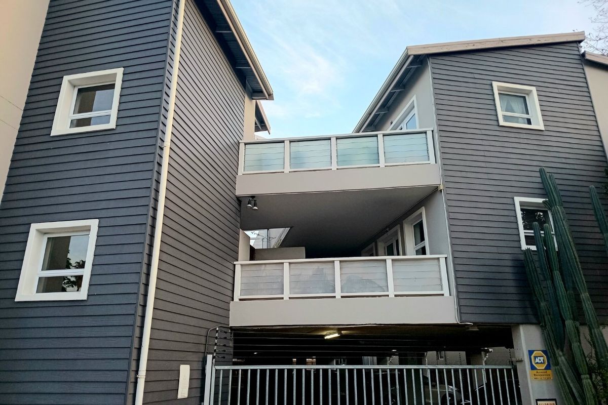 Exterior view of an apartment building featuring dark weatherboard cladding, stacked balconies with glass balustrades, and secure gated parking access.