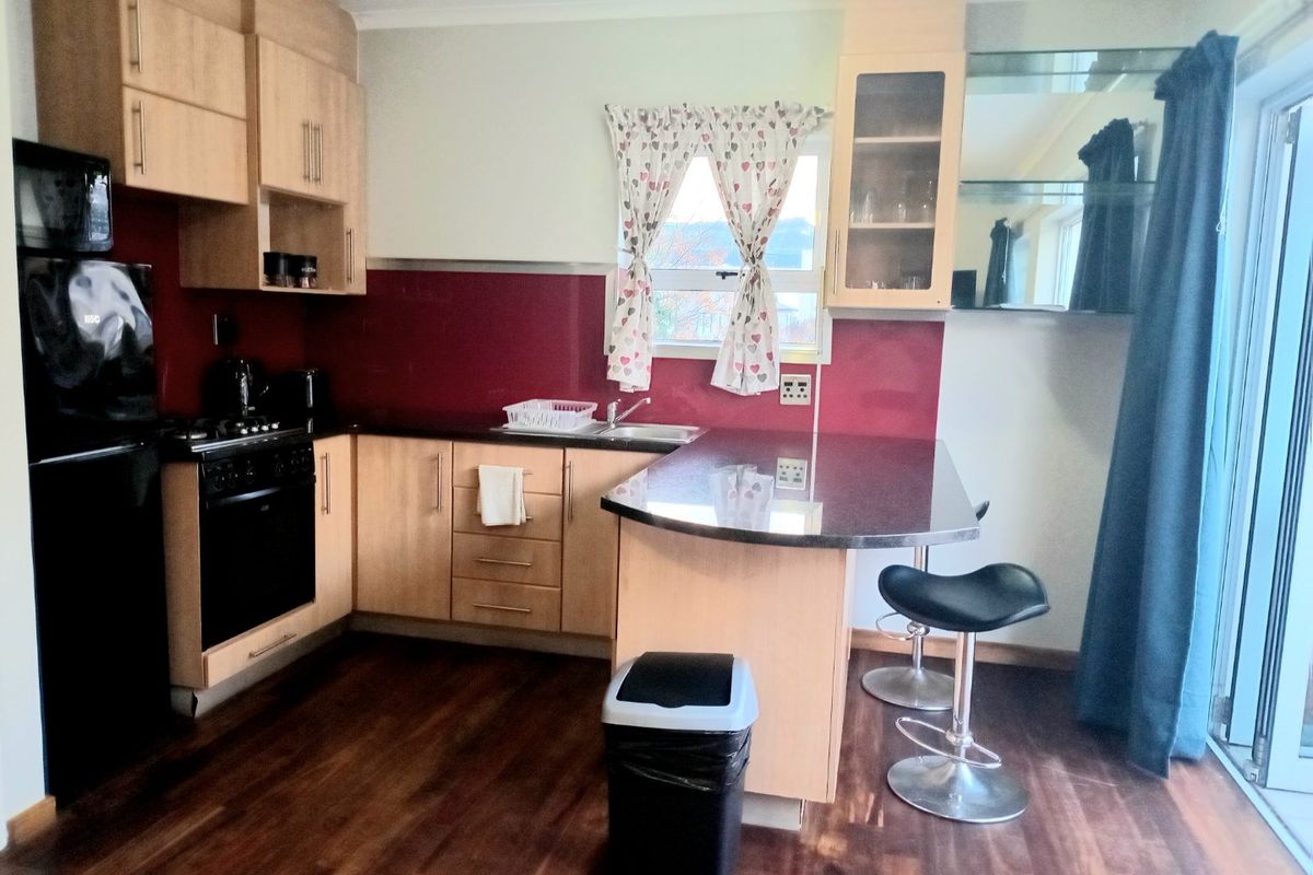 A functional kitchen featuring light wood cabinetry, dark countertops, a breakfast bar, and integrated cooking appliances with a red splashback.