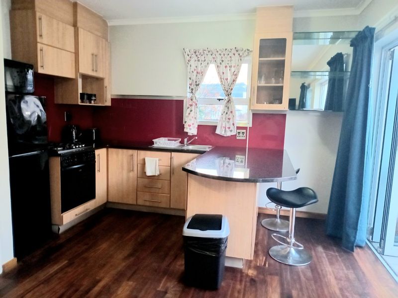 A functional kitchen featuring light wood cabinetry, dark countertops, a breakfast bar, and integrated cooking appliances with a red splashback.