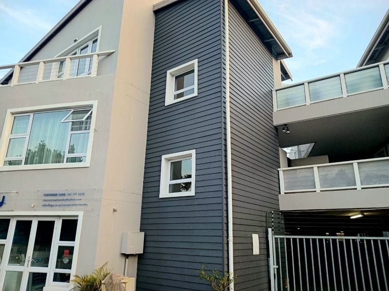 A modern apartment building exterior featuring dark horizontal cladding, white window frames, and multiple balconies with metal railings.