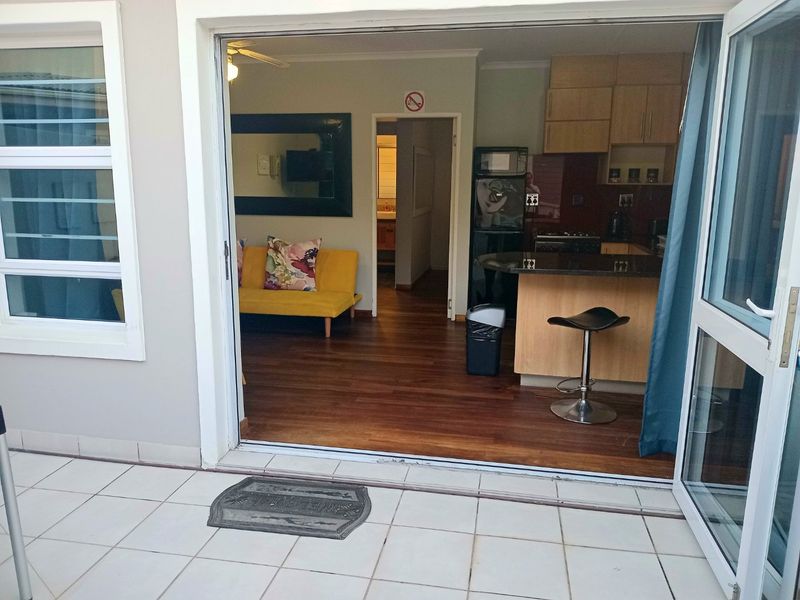 Open plan living area and kitchen with laminate flooring, leading out to a tiled patio through double glass sliding doors.
