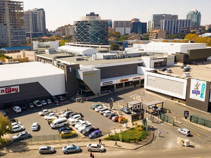 Aerial view of a commercial shopping center complex featuring extensive parking facilities, retail storefronts, and surrounding urban infrastructure.