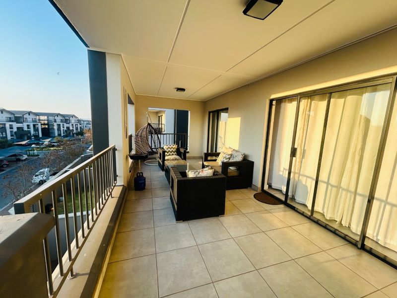 A spacious covered balcony featuring tiled flooring, metal railings, and large sliding glass doors providing access to the interior living area.