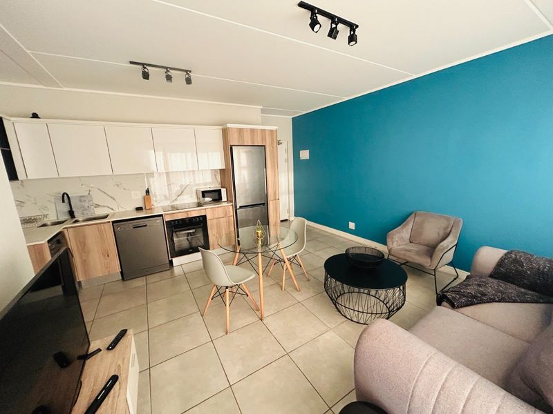 Modern open-plan apartment living area featuring a contemporary kitchen with wood-finish cabinetry, marble-look splashback, and integrated appliances, seamlessly flowing into the lounge space.