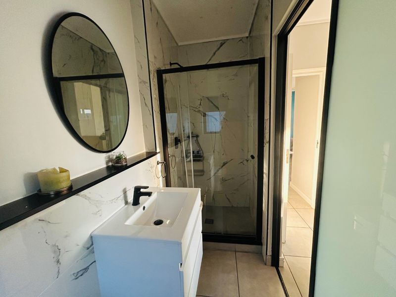 Modern bathroom featuring a sleek vanity with black mixer tap, marble-look wall tiling, and a glass-enclosed shower with black framing.