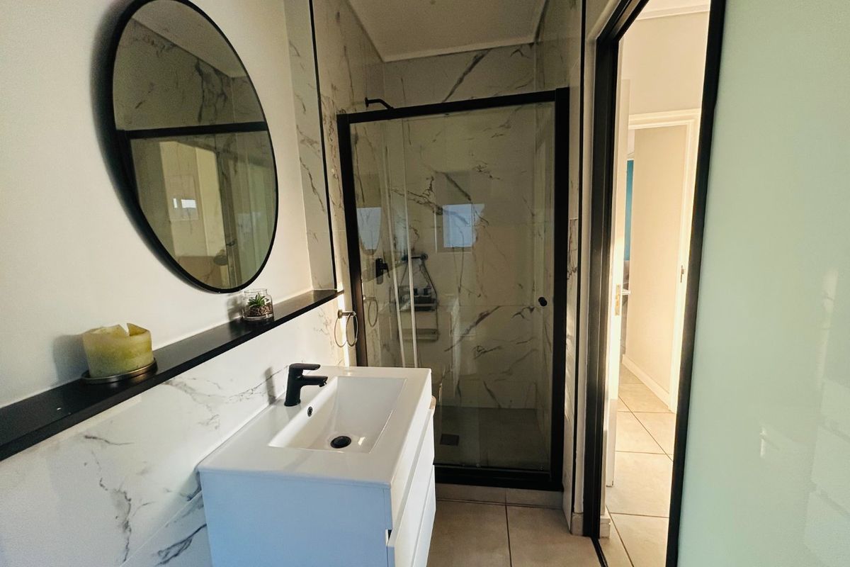 Modern bathroom featuring a sleek vanity with basin, marble-look wall tiling, and a glass-enclosed shower with black frame detailing.