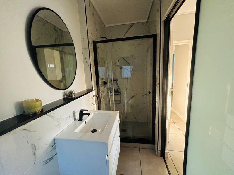 Modern bathroom featuring a sleek vanity with basin, marble-look wall tiling, and a glass-enclosed shower with black frame detailing.
