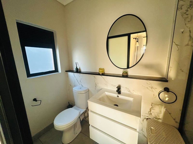 Modern bathroom featuring marble-look wall tiles, a sleek vanity with black tapware, a circular mirror, and a floating shelf.
