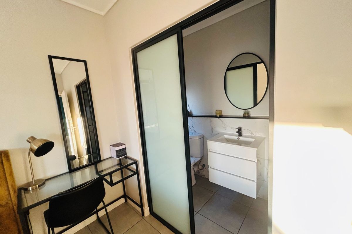 A modern bedroom featuring a sleek sliding glass door leading to an en-suite bathroom with a contemporary vanity and marble-look wall tiles.