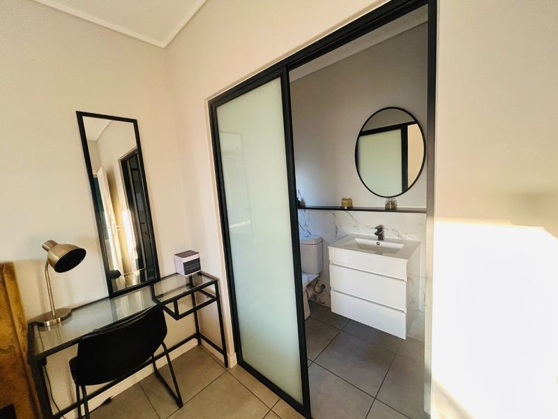A modern bedroom featuring a sleek sliding glass door leading to an en-suite bathroom with a contemporary vanity and marble-look wall tiles.