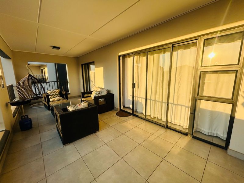 A spacious covered balcony featuring large sliding glass doors, neutral tiled flooring, and modern aluminium window frames, perfect for outdoor relaxation.