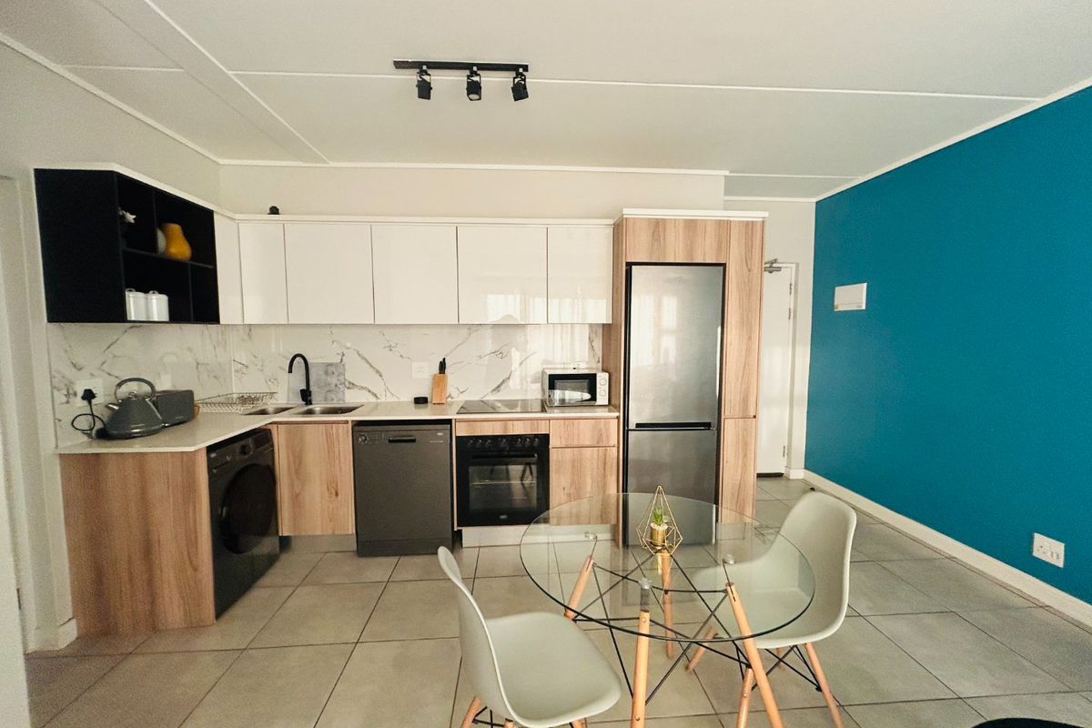Modern open-plan kitchen featuring wood-tone and white cabinetry, marble-look splashback, integrated appliances, and tiled flooring, seamlessly flowing into the living area.