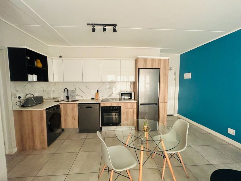 Modern open-plan kitchen featuring wood-tone and white cabinetry, marble-look splashback, integrated appliances, and tiled flooring, seamlessly flowing into the living area.