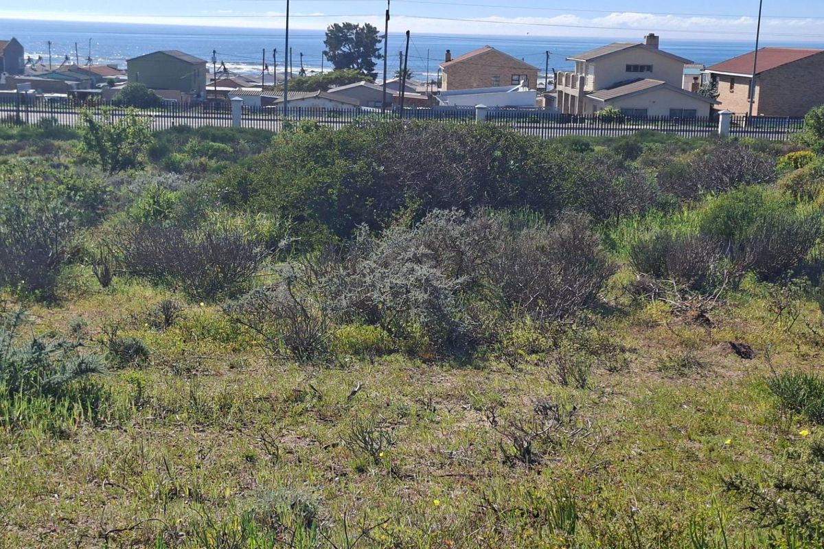 A vacant residential plot featuring natural coastal vegetation and perimeter fencing, offering a clear view of the surrounding neighborhood and the ocean.