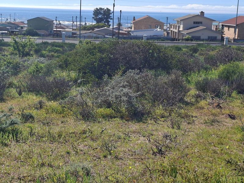 A vacant residential plot featuring natural coastal vegetation and perimeter fencing, offering a clear view of the surrounding neighborhood and the ocean.