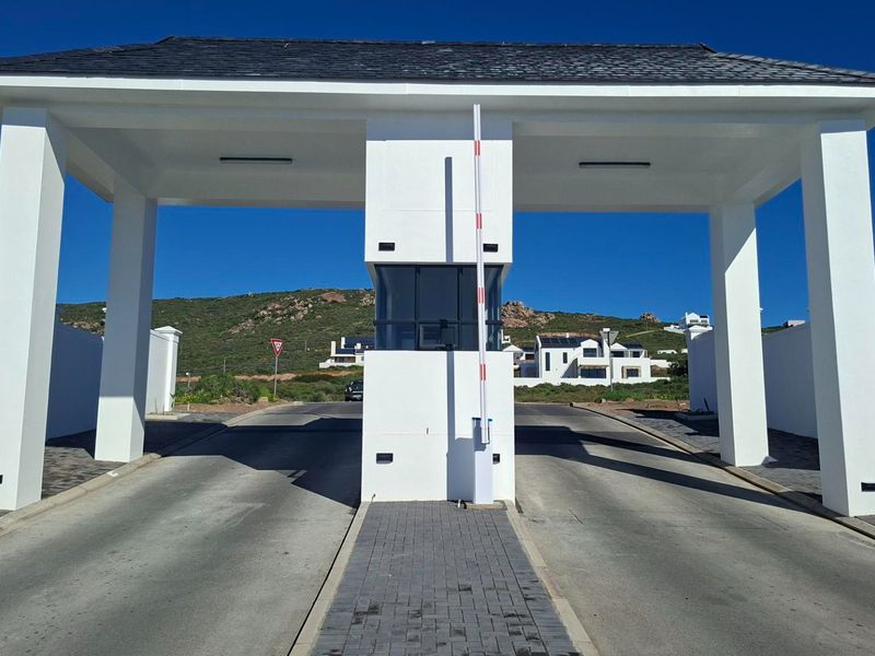 A modern, well-maintained security gatehouse entrance for a residential estate, featuring a boom gate, paved driveway, and clean architectural lines.