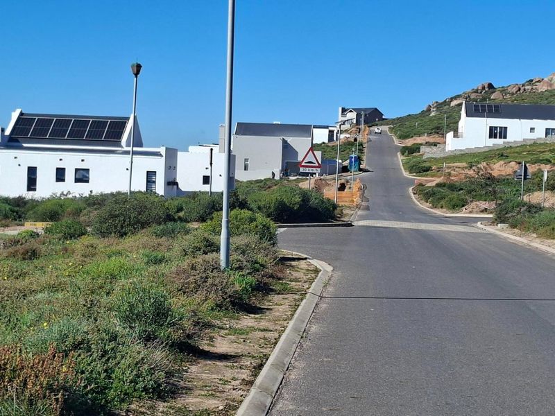 A view of the paved residential street and surrounding coastal landscape, showcasing the neighborhood approach and established modern homes.