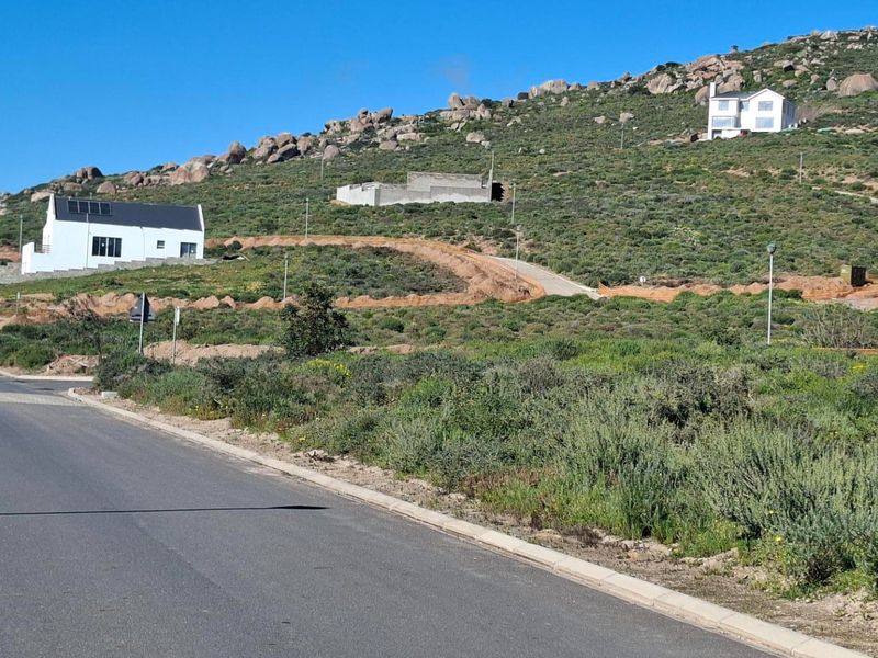 A street-level view of a residential development area featuring paved roads, street lighting, and surrounding hillside landscape with existing residential properties.