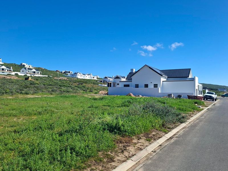 A vacant residential plot situated in a developed coastal estate, featuring established road infrastructure and surrounding modern residential properties.