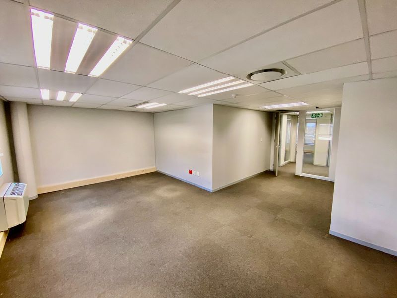 An empty commercial office space featuring a suspended ceiling, recessed lighting, carpeted flooring, and a glass partition entrance.