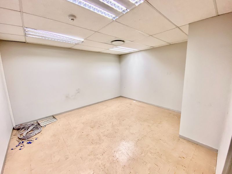 An empty commercial office space featuring a suspended ceiling, fluorescent lighting, and vinyl flooring, suitable for a variety of business configurations.