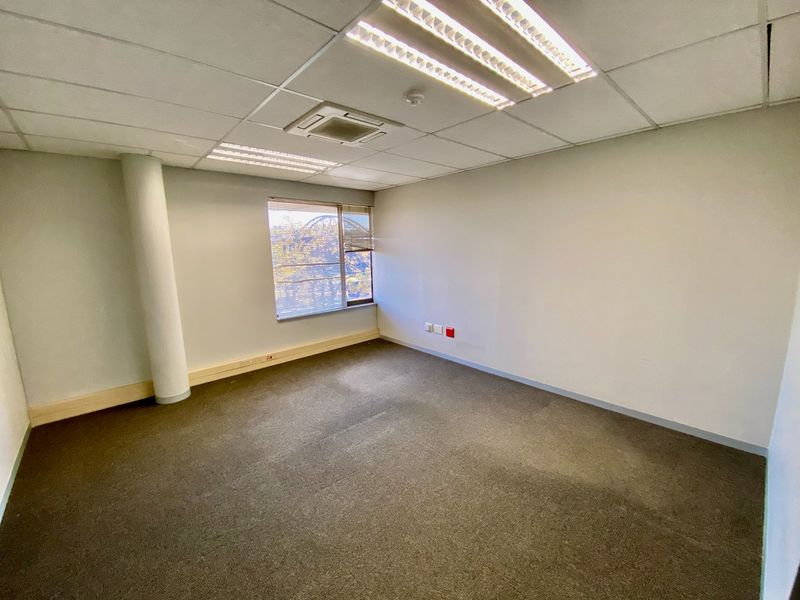 A vacant commercial office space featuring carpeted flooring, a suspended ceiling with recessed lighting, and a structural column.