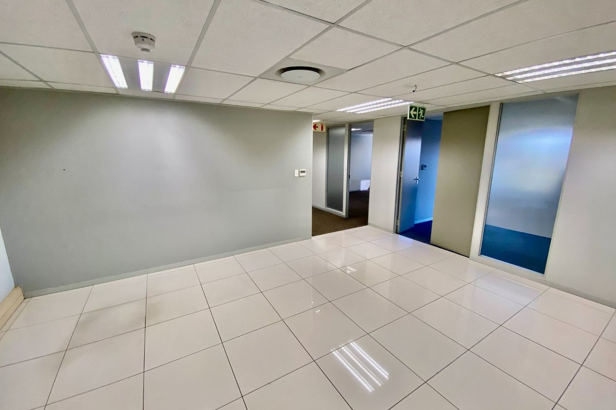 A vacant commercial office space featuring polished ceramic floor tiles, a suspended ceiling with recessed lighting, and glass partition doors leading to adjacent rooms.