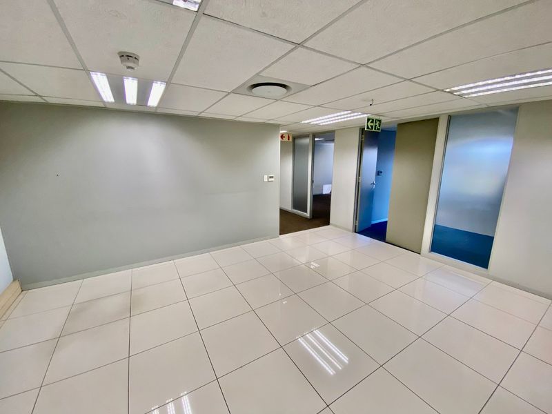 A vacant commercial office space featuring polished ceramic floor tiles, a suspended ceiling with recessed lighting, and glass partition doors leading to adjacent rooms.