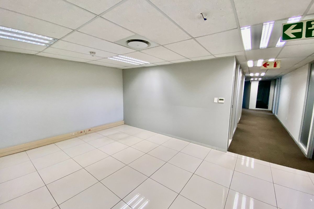 A vacant, well-maintained commercial office space featuring neutral grey walls, white ceramic floor tiles, and a suspended ceiling with integrated lighting.