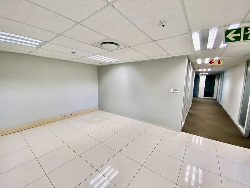 A vacant, well-maintained commercial office space featuring neutral grey walls, white ceramic floor tiles, and a suspended ceiling with integrated lighting.