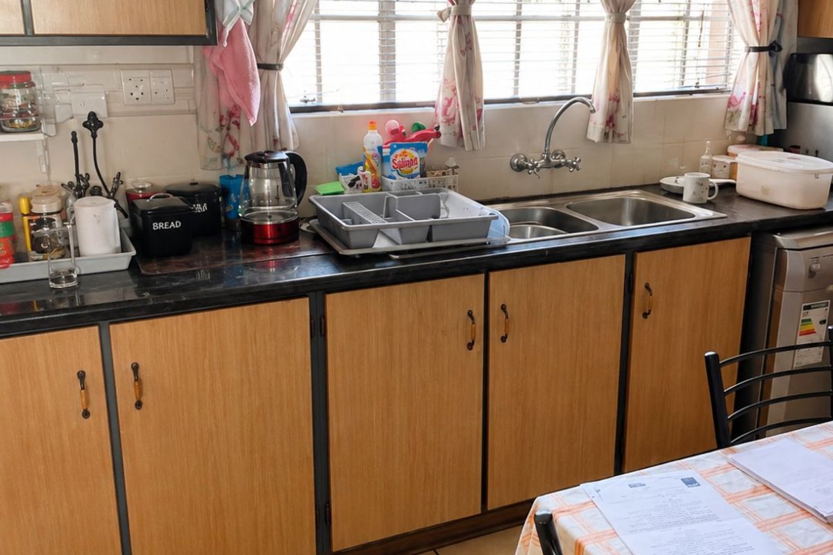 A functional kitchen featuring laminate cabinetry, a double basin sink, and tiled flooring, providing a practical workspace with natural light.