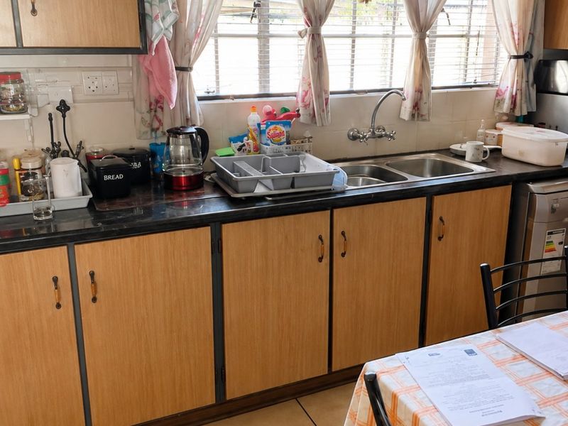 A functional kitchen featuring laminate cabinetry, a double basin sink, and tiled flooring, providing a practical workspace with natural light.