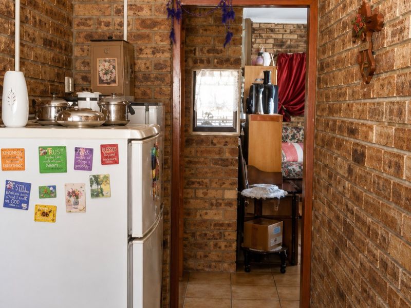 A narrow hallway featuring exposed brick walls and ceramic floor tiles, providing a rustic aesthetic and connecting to adjacent living spaces.
