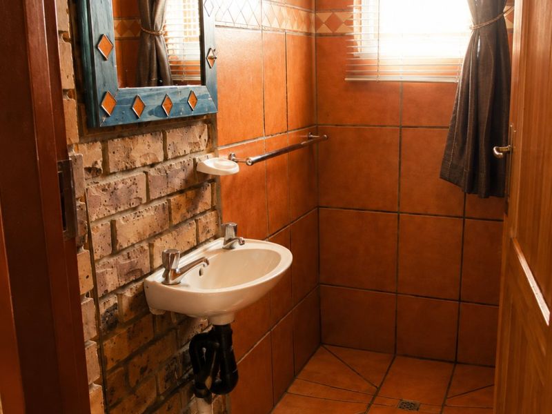 Compact bathroom featuring rustic exposed brick walls, terracotta-style floor and wall tiling, a wall-mounted basin, and a tiled shower area.