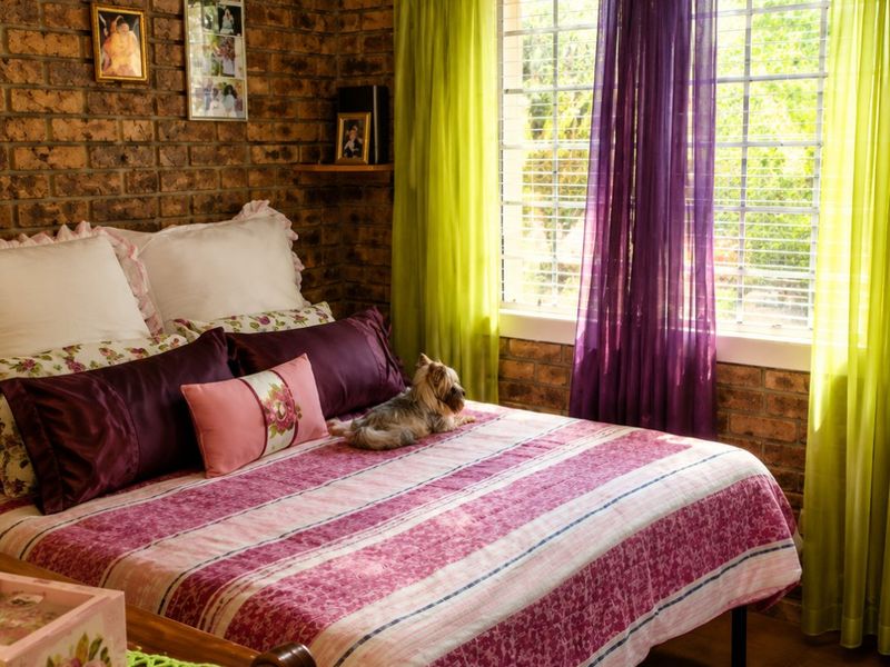 A bedroom featuring rustic exposed brick walls, tiled flooring, and a window fitted with security bars, offering a warm and textured aesthetic.