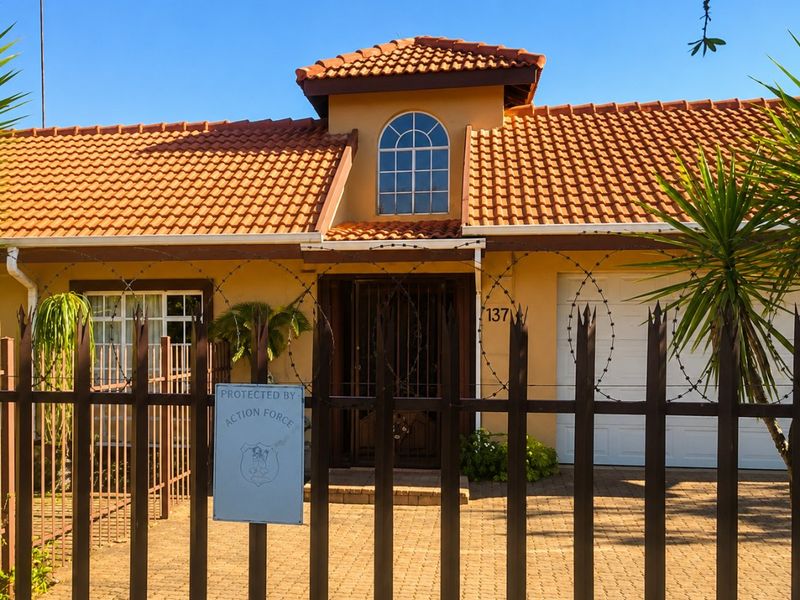 Front elevation of a commercial property featuring a terracotta tiled roof, arched window, paved driveway, and secure metal perimeter fencing with razor wire.